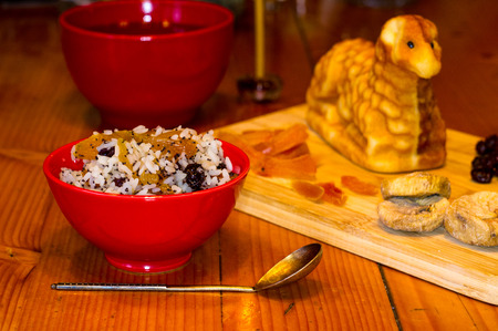 preparation of treats for traditional Orthodox Christmas - handmade baked cookies in the form of lambkin, dried fruits, cranberries, honey, nuts, rice pudding, mortar with poppy seeds, Church candles on a wooden tableの写真素材