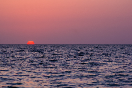 Summer sea sunset on the pebble beach, the sun, waves and clouds, beautiful dramatic lightingの写真素材