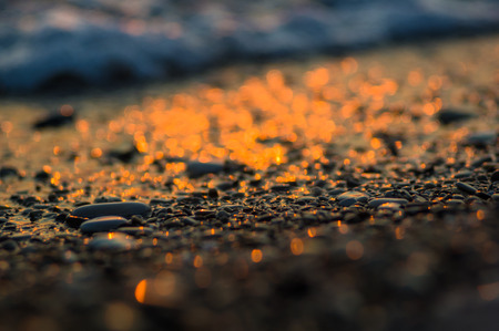 pebble stones on the sea beach on a warm summer evening at sunset, the rolling waves of the blue sea...