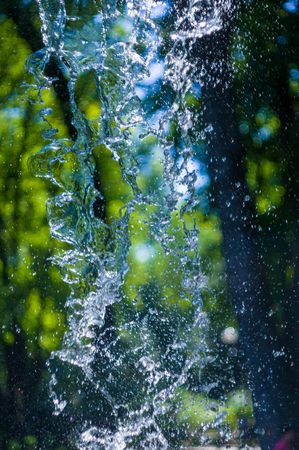 transparent falling water vertical flows against a blue sky and green landscape, close-upの写真素材