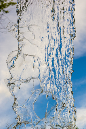 transparent falling water vertical flows against a blue sky and green landscape, close-upの写真素材