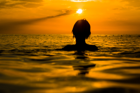 Girl swimming in the sea at sunset, splashes of transparency water, female silhouetteの写真素材