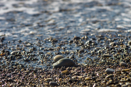 pebble stones on the sea beach on a warm summer day, the rolling waves of the blue sea with white foamの写真素材