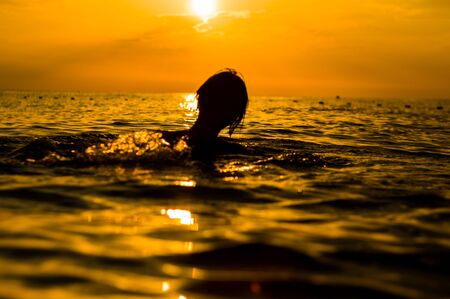 Girl swimming in the sea at sunset, splashes of transparency water, female silhouetteの写真素材