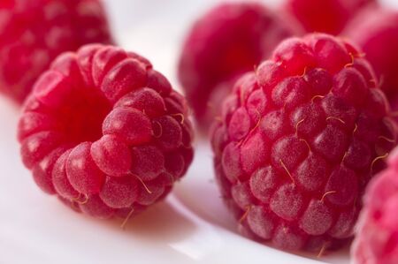 big fresh juicy raspberries on a white saucer close up, selected focusの写真素材