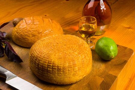still life - national Adyghe cheese homemade on a cutting Board with a knife, Basil, parsley, lime, sesame oil, chili pepper, macadamia nuts and a decanter on a wooden table, close-upの写真素材