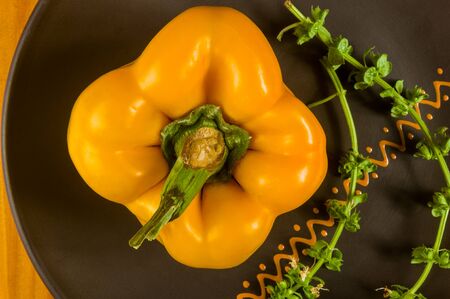 a freshest yellow paprika, bell pepper in ceramic plate with basil flowers on wooden background, close upの写真素材