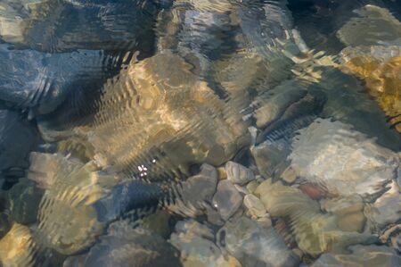 pebble stones on the sea beach on a warm summer day, the rolling waves of the blue sea with white foamの写真素材