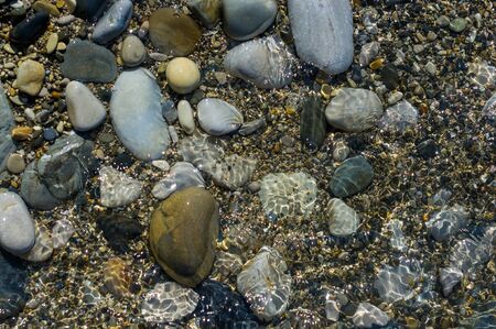 pebble stones on the sea beach on a warm summer day, the rolling waves of the blue sea with white foamの写真素材