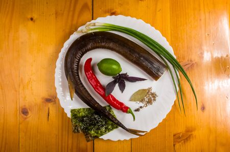 still life - smoked garfish with lime, Basil, green onions, chili, nori chips, spices, olive oil in a white ceramic dish, on a wooden tableの写真素材