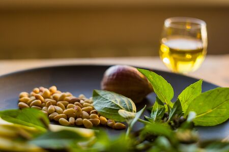 Fresh ingredients for preparing Italian pesto sauce - lemon basil sprigs, peeled seeds of cedar nuts, large garlic clove, Greek olive oil, Parmesan cheese, on a ceramic plate, in scattered sunlightの写真素材