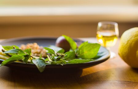 Fresh ingredients for preparing Italian pesto sauce - lemon basil sprigs, peeled seeds of cedar nuts, large garlic clove, Greek olive oil, Parmesan cheese, on a ceramic plate, in scattered sunlightの写真素材