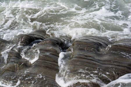 pebble stones on the sea beach on a warm summer day, the rolling waves of the blue sea with white foamの写真素材