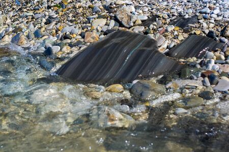pebble stones on the sea beach on a warm summer day, the rolling waves of the blue sea with white foamの写真素材