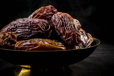 Big luxury dried date fruit in bowls on the dark surface, kurma ramadan kareem concept.