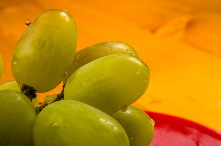 still life - a large brush of green grapes with water drops in a red ceramic plate on a wooden backgroundの写真素材