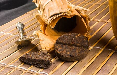 Chinese pressed PU-erh tea in bamboo leaf packaging and tea accessories on a bamboo Mat, close-upの写真素材