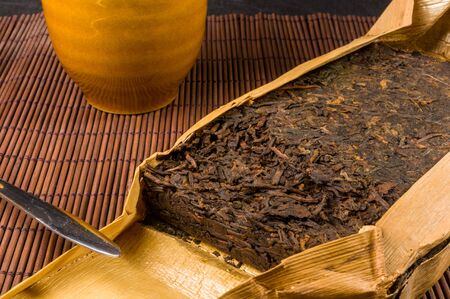 Chinese pressed PU-erh tea in bamboo leaf packaging and tea knife on a bamboo Mat, close-up