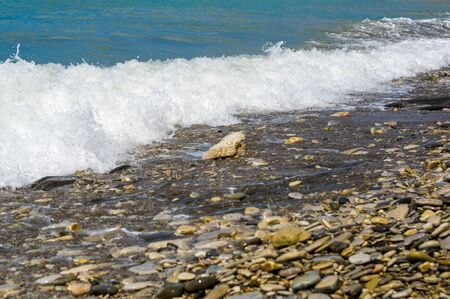 pebble stones on the sea beach on a warm summer day, the rolling waves of the blue sea with white foamの写真素材