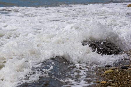 pebble stones on the sea beach on a warm summer day, the rolling waves of the blue sea with white foamの写真素材