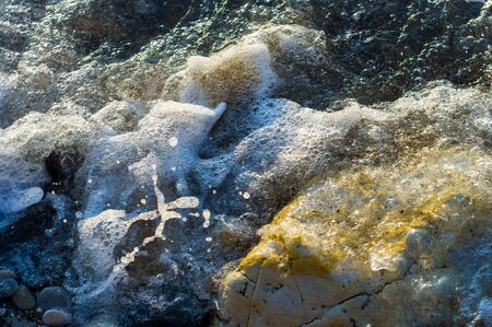 pebble stones on the sea beach on a warm summer day, the rolling waves of the blue sea with white foamの写真素材