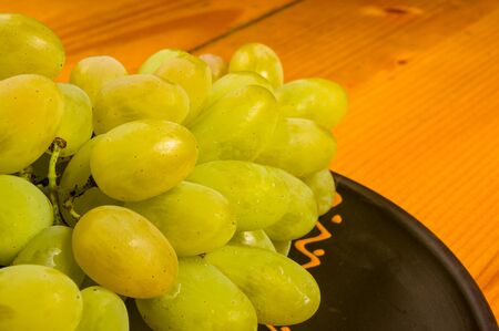 still life - a large brush of green grapes in a dark ceramic plate on a wooden backgroundの写真素材