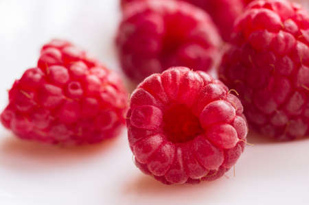 big fresh juicy raspberries on a white saucer close up, selected focusの写真素材