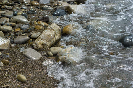 pebble stones on the sea beach on a warm summer day, the rolling waves of the blue sea with white foamの写真素材