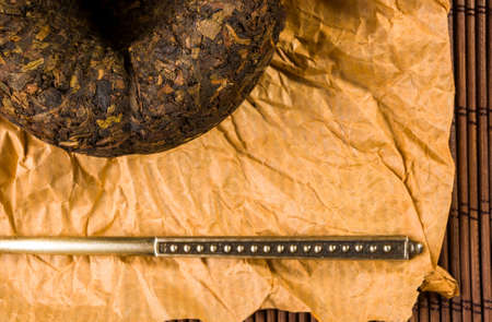 Chinese pressed PU-erh tea on wrapping paper and tea accessories on a bamboo Mat, close-up