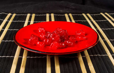Sweet dried cherries in a red saucer on a bamboo mat, close up.の写真素材