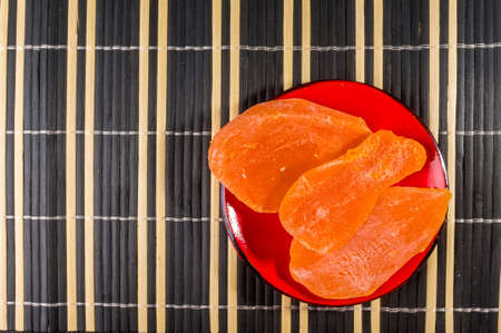 Large slices of dried mango in a red saucer on a bamboo mat, close up.の写真素材