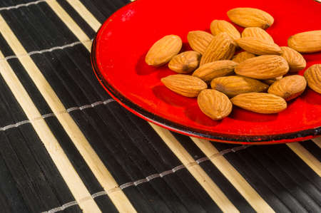 Almonds nuts in a red saucer on a bamboo mat, close up.の写真素材