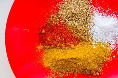 Spices - red paprika, ground coriander, salt and turmeric on a red plate, close upの写真素材