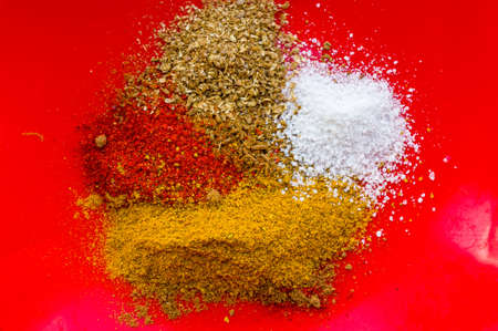 Spices - red paprika, ground coriander, salt and turmeric on a red plate, close upの写真素材