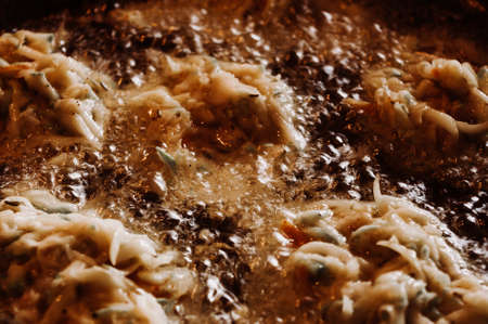 Fried vegetable fritters with zucchini, carrots, herbs, eggs, seasonings and cheese in boiling oil, close-up, selective focusの写真素材