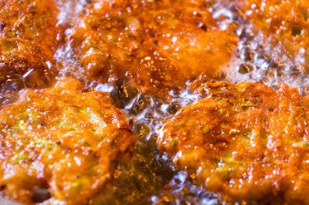 Fried vegetable fritters with zucchini, carrots, herbs, eggs, seasonings and cheese in boiling oil, close-up, selective focusの写真素材
