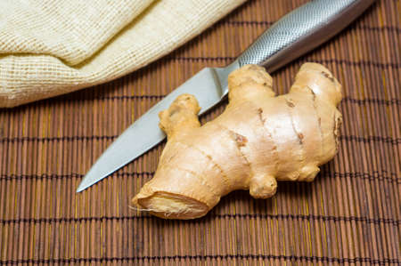 fresh ginger root on bamboo mat with knife and napkin, closeup
