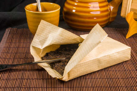 Chinese pressed PU-erh tea on wrapping paper and tea accessories on a bamboo Mat, close-upの写真素材