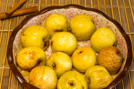 Baked apples with cinnamon in a ceramic bowl on a bamboo mat, close upの写真素材