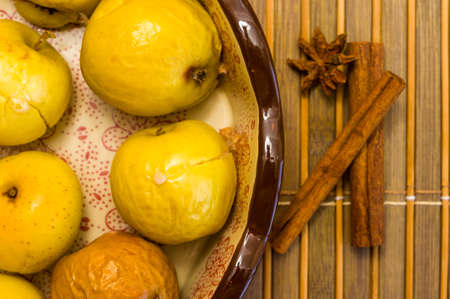 Baked apples with cinnamon in a ceramic bowl on a bamboo mat, close upの写真素材