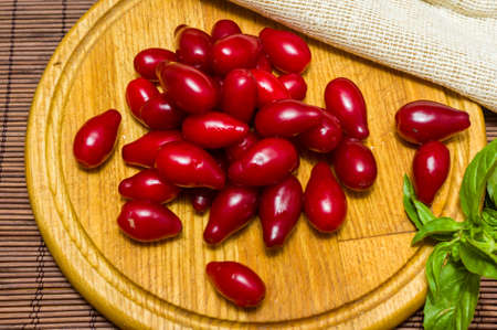 Still life - fresh large dogwood berries, purple plums and a sprig of basil on a wooden board, close upの写真素材