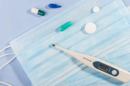 Background concept for news about the novel coronavirus COVID-19 pandemic, antiviral medical mask for protection against coronavirus. Surgical protective mask. Medical respiratory bandage face and thermometer, lettering on copy space.の写真素材