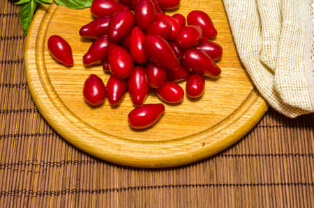 Still life - fresh large dogwood berries, purple plums and a sprig of basil on a wooden board, close upの写真素材