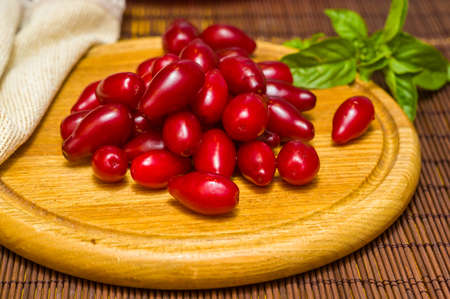 Still life - fresh large dogwood berries, purple plums and a sprig of basil on a wooden board, close upの写真素材
