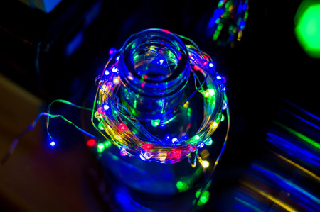 Glowing Christmas multicolored LED garland in a glass bottle, black background, macro, close-upの写真素材