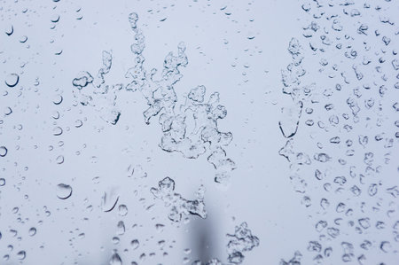 Melting snow on the glass, drops of water condensation on the window, and transparent glass of the window in cold winter, winter landscape outside the window, close-upの写真素材