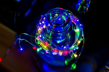 Glowing Christmas multicolored LED garland in a glass bottle, black background, macro, close-upの写真素材