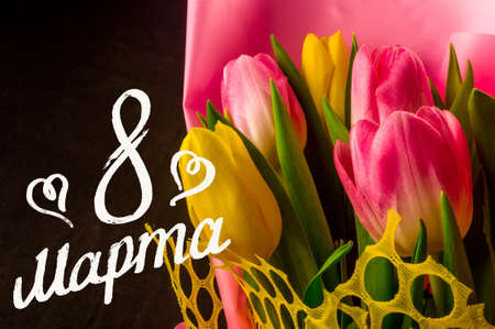 Greeting card - a bouquet of fresh spring pink and yellow tulips, holiday greetings, handwritten inscription with a brush 8 march, greeting lettering, russian text. Text translation - 8 march.の写真素材