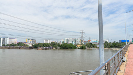 Image of high-voltage power lines crossing a large river. There are many buildings and commercial buildings surrounding it. At the river bank there are trees growing in spots. On tの写真素材