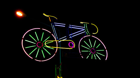 Image of multi-colored neon bulbs which was modified into the shape of a two-wheeled yellow bicycle. There is a seat in the back so you can sit in the back. Standing on a pole in tの写真素材